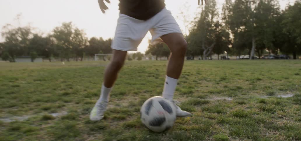 A teenager plays soccer in a field at sunset