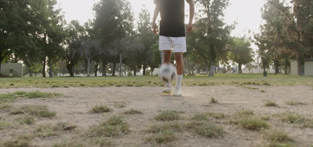 Man kicks a soccer ball in a field under a sunny sky