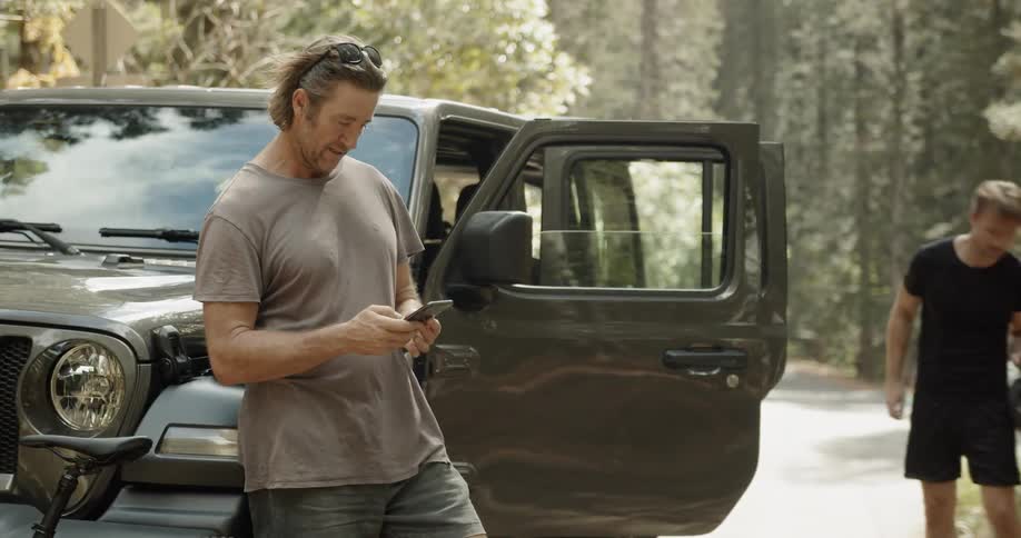Man types on his phone next to a parked car