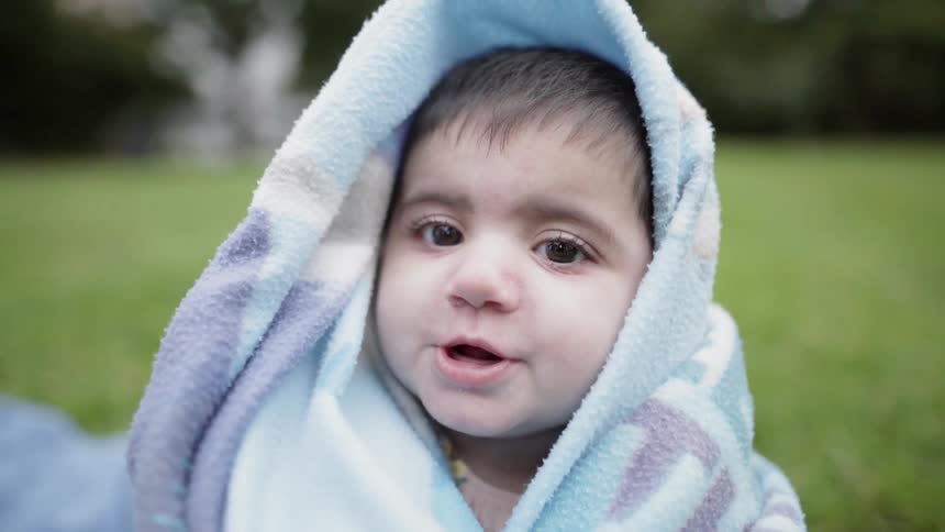 Baby is wrapped in blanket and sitting in the grass