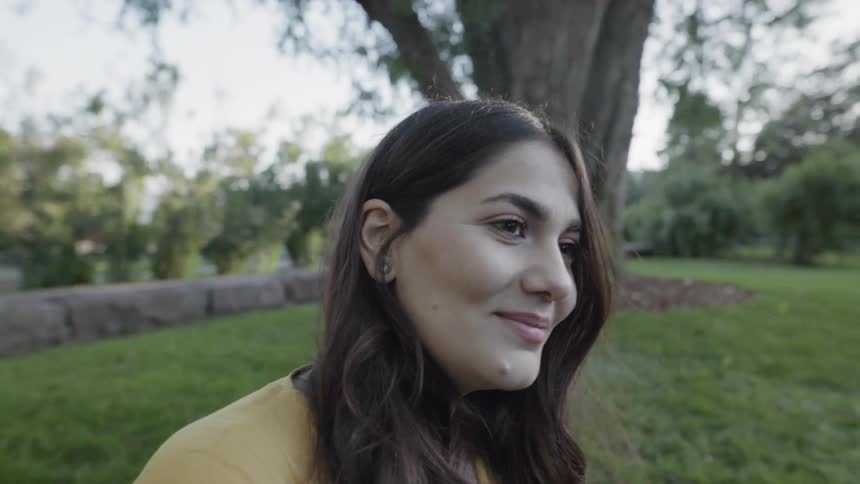 A beautiful young woman in a yellow outfit smiling outdoors in park lawn.