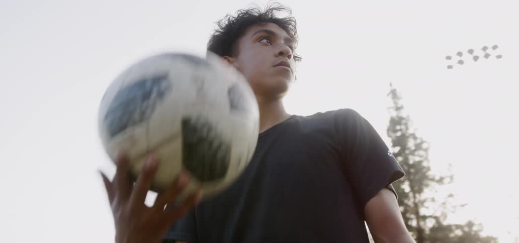 A teenager tosses and catches a soccer ball on a sunny day