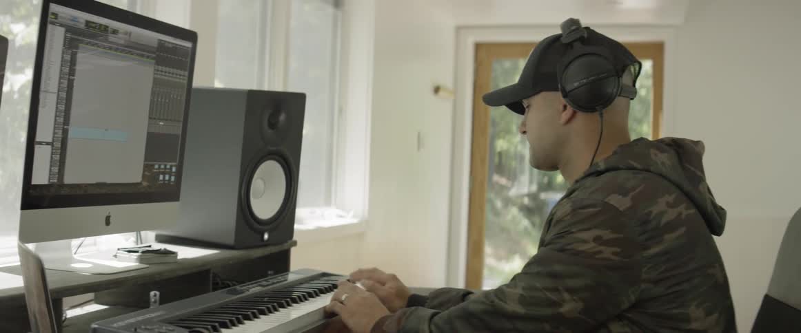 Man plays a piano in front of speakers and a monitor