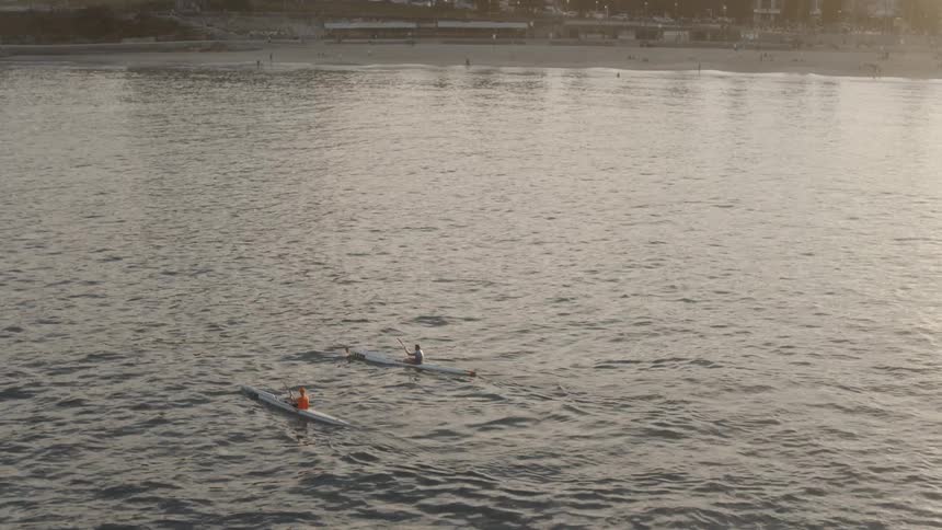 People kayak just off the coast at sunset