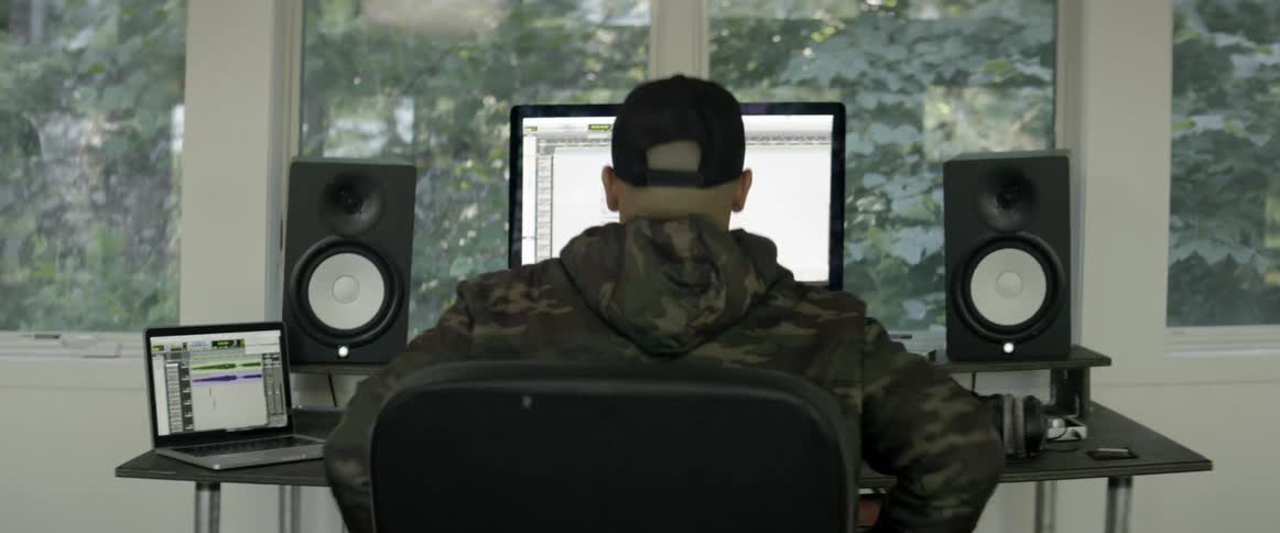 A man sits down at a desk with music recording equipment