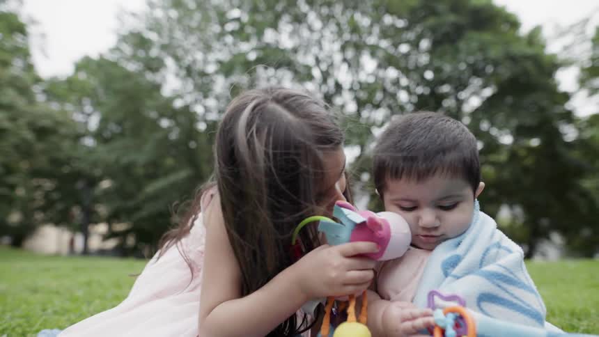 A girl and baby play on a blanket on a lawn