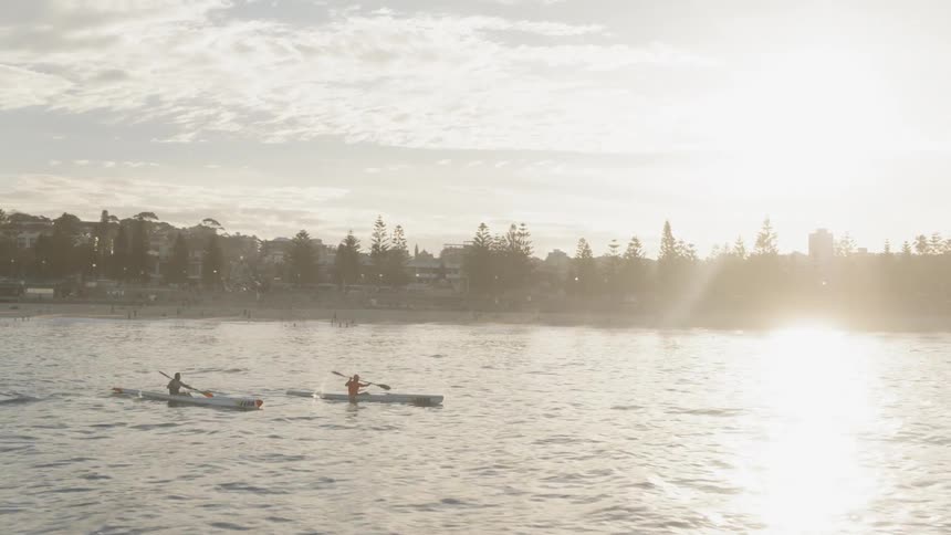 Two people kayak on a lake at sunset