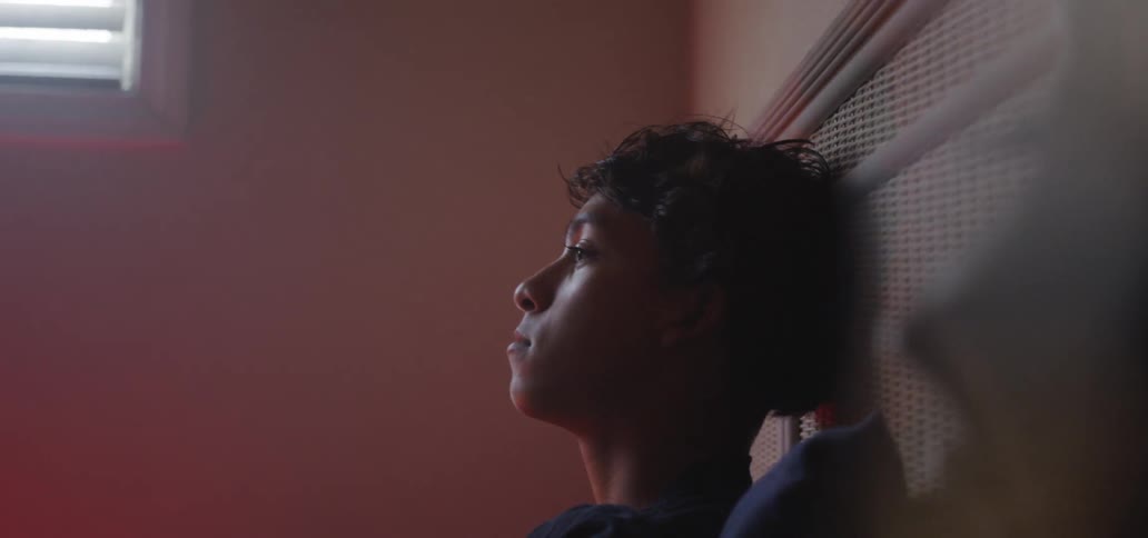 A boy is sitting on his bed in daylight thinking
