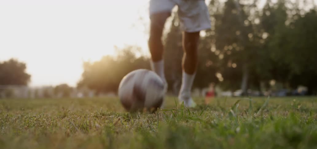 A boy dribbles then kicks a soccer ball on a grassy field