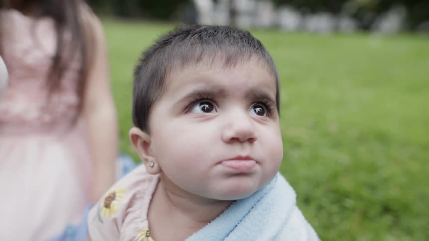 Girl and baby sit outside on the grass