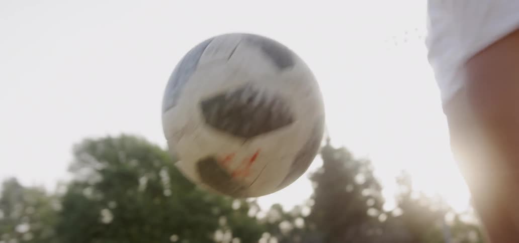 A teenager plays soccer in a field at sunset