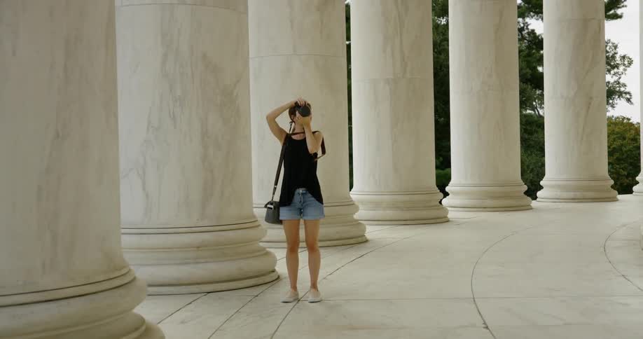 A woman is touring and taking photos of a large building in Washington DC with white stone pillars