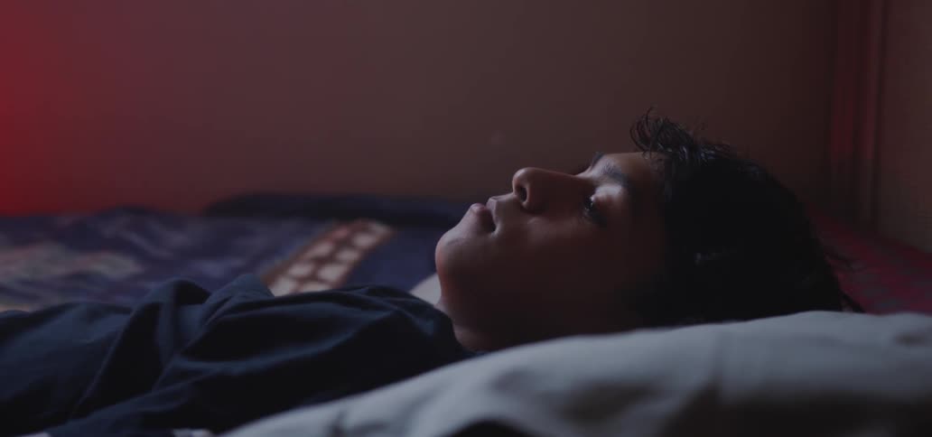 Young boy blinks his eyes as he lays on the bed