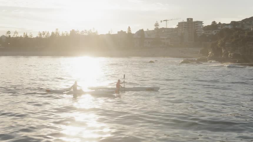Two men kayak just off the coast at sunset