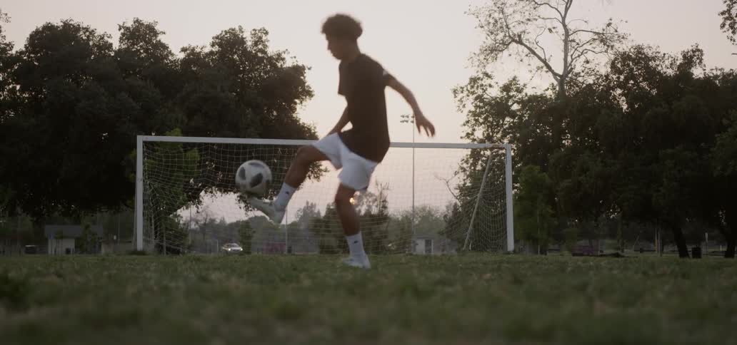 A teenager plays soccer in a field at sunset