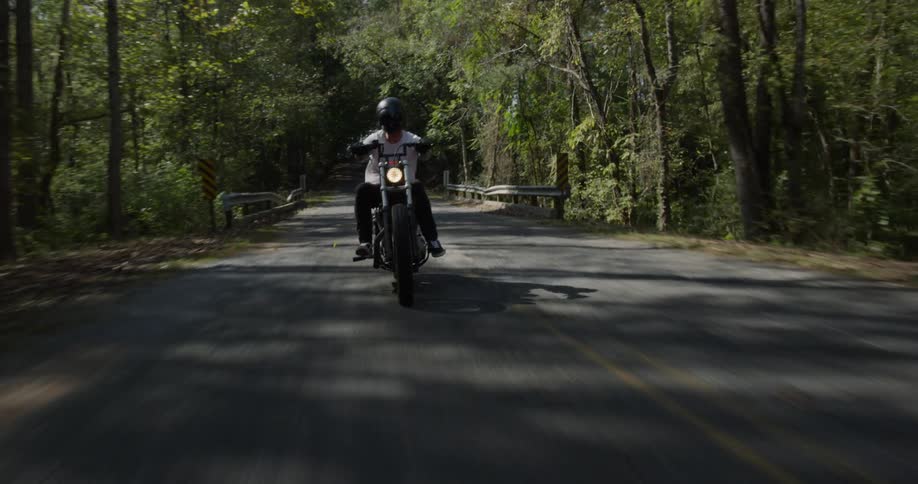 Man is riding motorcycle on highway surrounded by trees