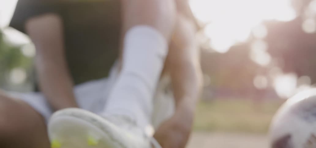 An athlete puts on a cleat while sitting on grass