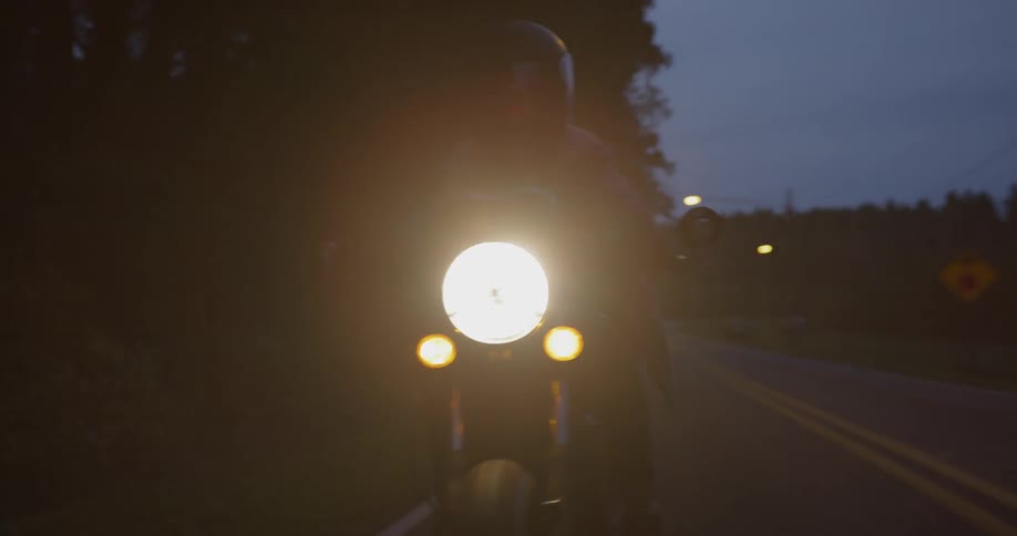 A motorcyclist rides on a rural road at night
