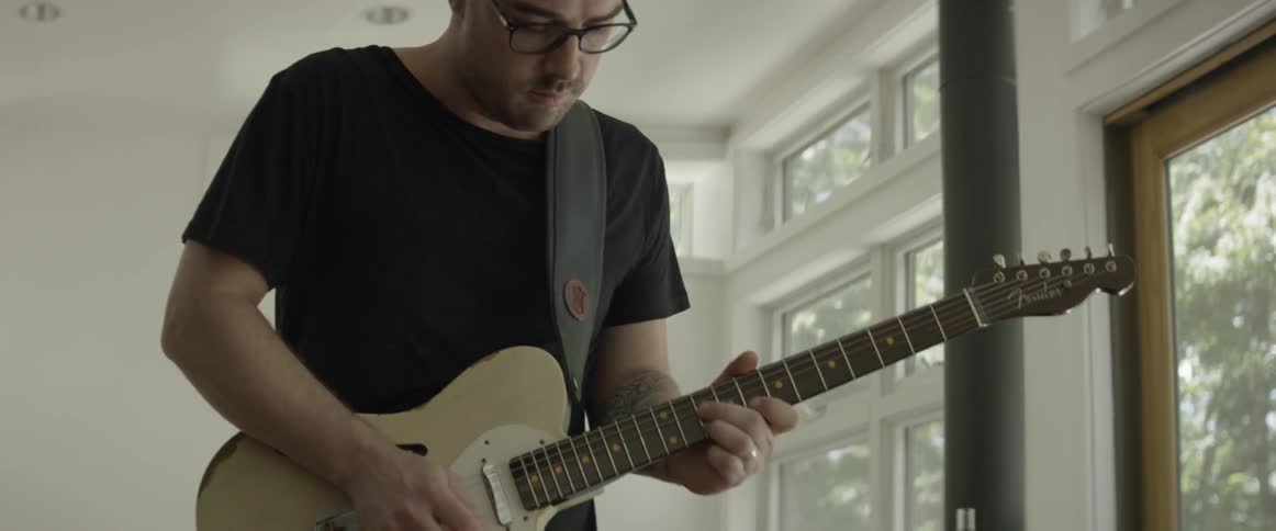 A man is playing a guitar inside a room in daylight