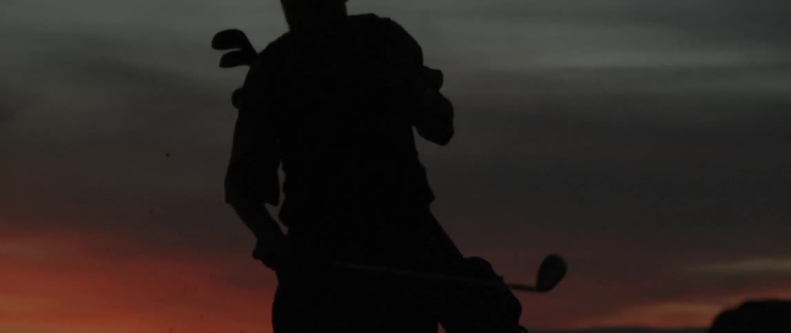 Man carries golf clubs as he walks
