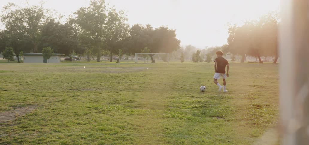 Boy is kicking a soccer ball in an open soccer field as suns ets
