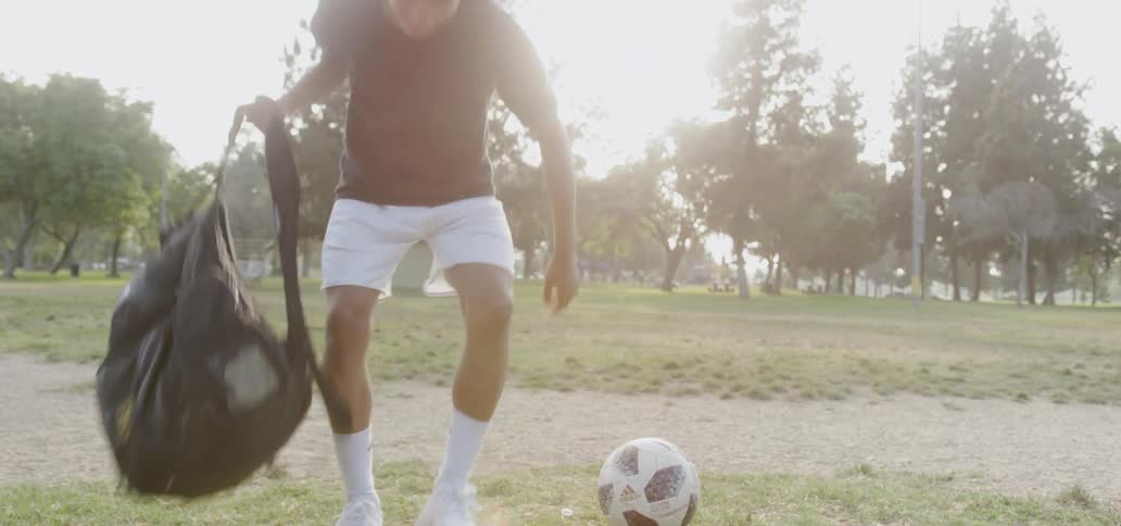 A teenager plays soccer in a field on a sunny day