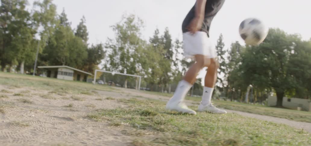 Young man juggling a soccer ball on a patchy field near sunset