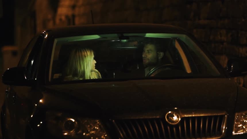 A man and woman talk in a parked car at night