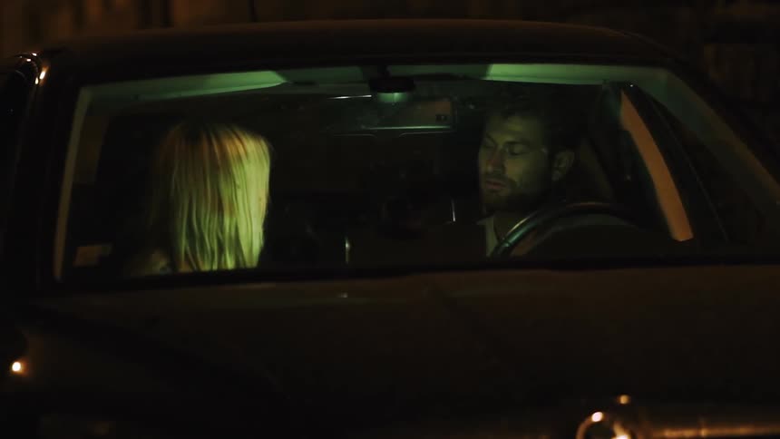 A man and woman talk in a parked car at night