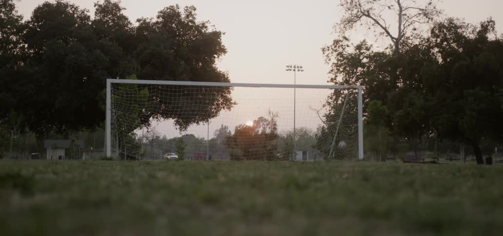 boy runs in a field and kicks a soccer ball into a net
