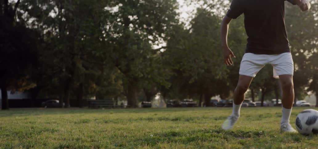 A teenager plays soccer in a field at sunset
