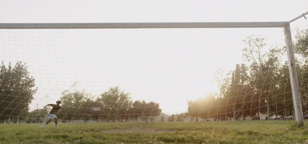 Man kicks a soccer ball into the net