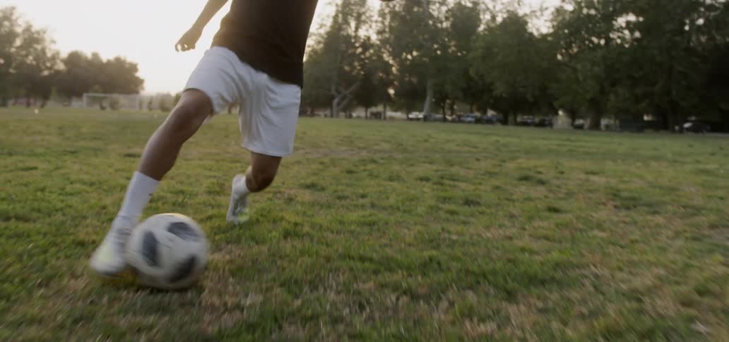 A teenager plays soccer in a field at sunset