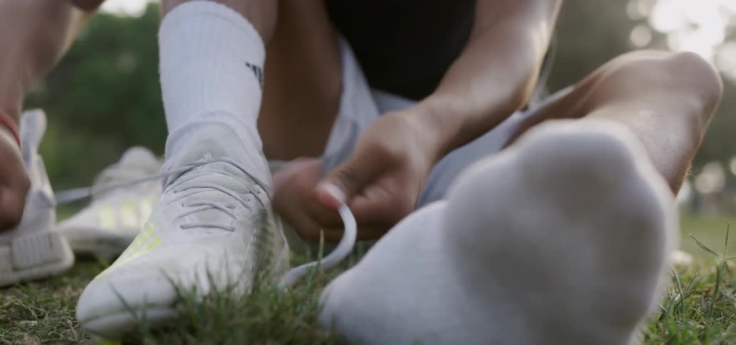 Person is sitting in grass outside and tying cleats