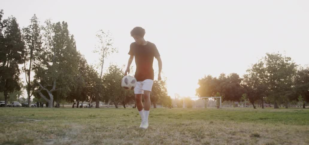 A teenager plays soccer in a field at sunset
