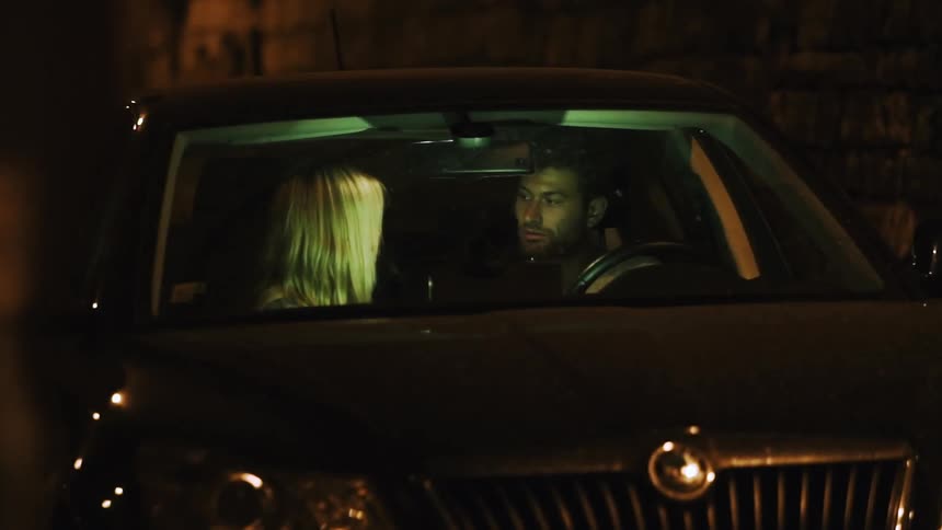 A man and woman talk in a parked car at night