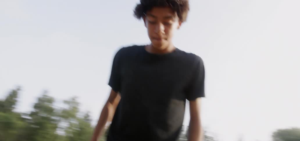 A boy dribbles and kicks a soccer ball up into his hands on a field