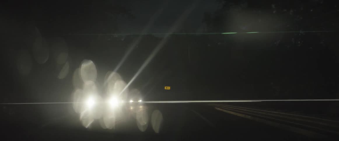 Bright headlights shine as cars pass on a dark road at night