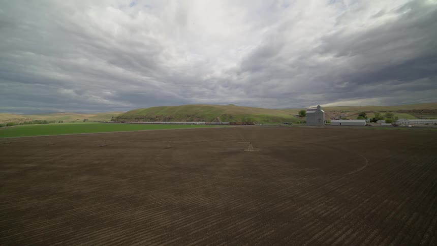 Ultra wide converge of a freight train traveling through farmland under stormy skies