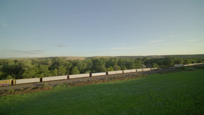 Slow push toward a freight train traveling between woods and a corn field