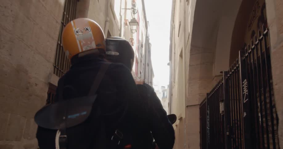 Man and woman ride a motorcycle between the buildings in a city