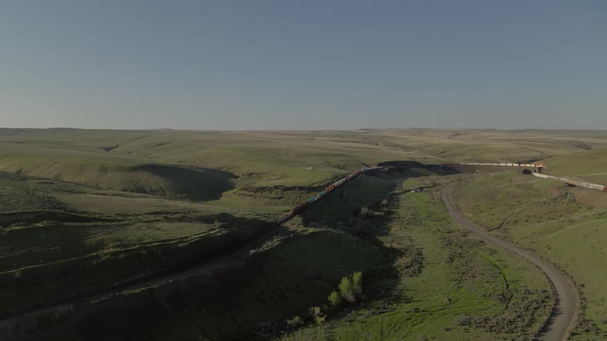Wide shot of a long freight train descending a steep grade amidst rolling hills