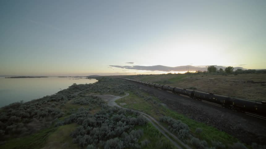 Converging with an oil freight train near a river at sunset