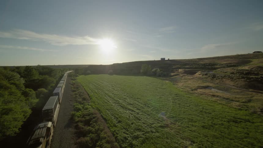 Flying over a container train as it travels through sunny and lush countryside