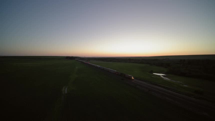 Wide overview of a freight train running through lush open farm country at dusk
