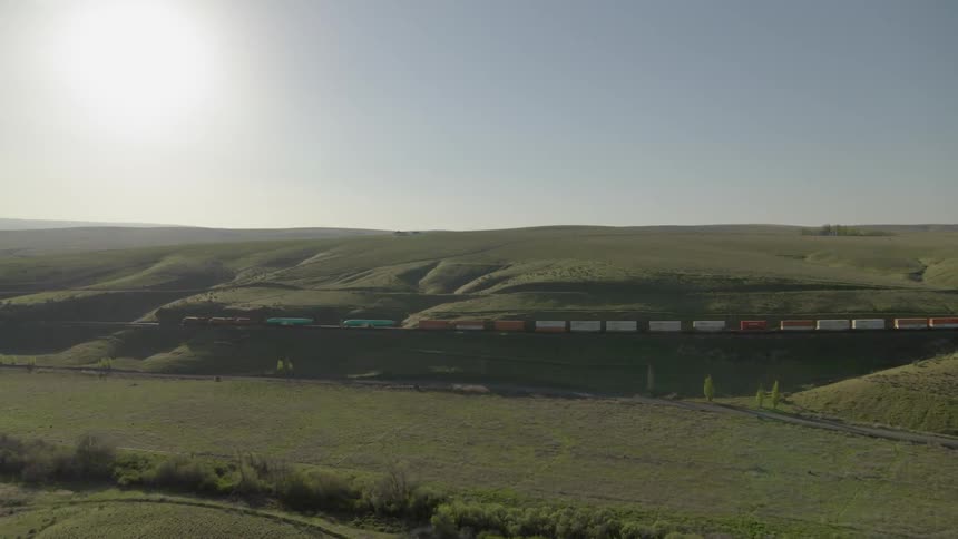 A freight train travels along grassy hills