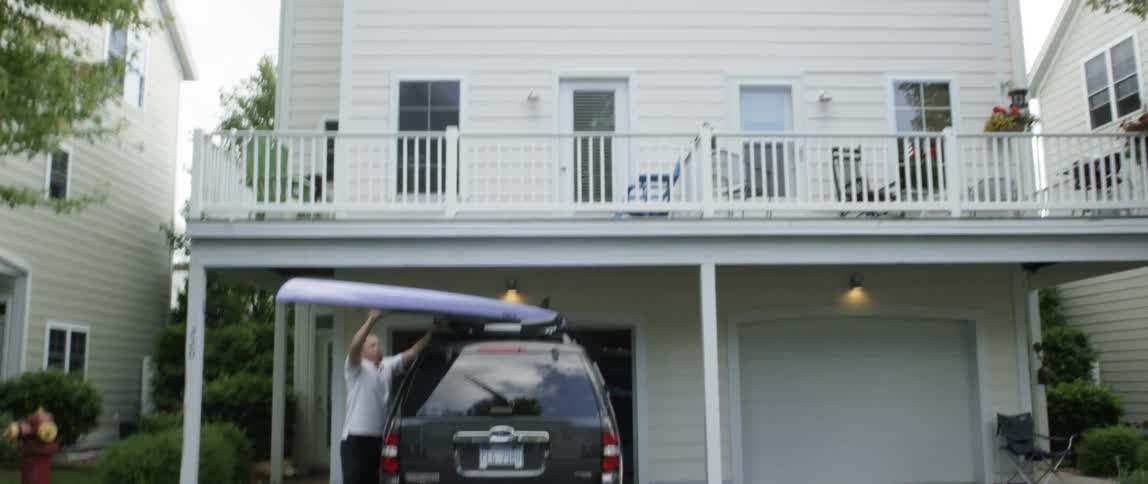 A man puts a surfboard on a car rooftop