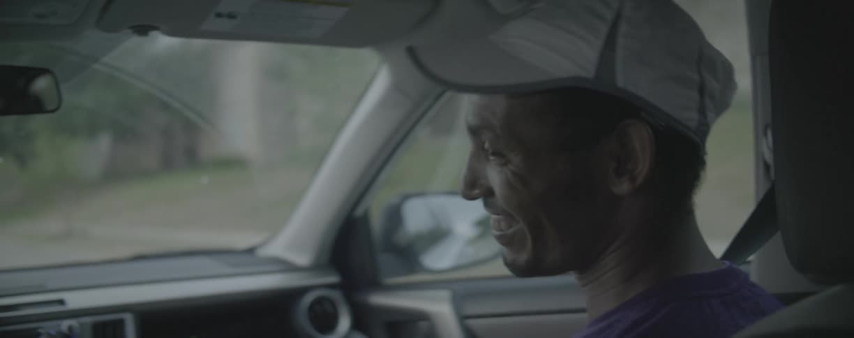 A man riding in a car smiles and nods toward the driver