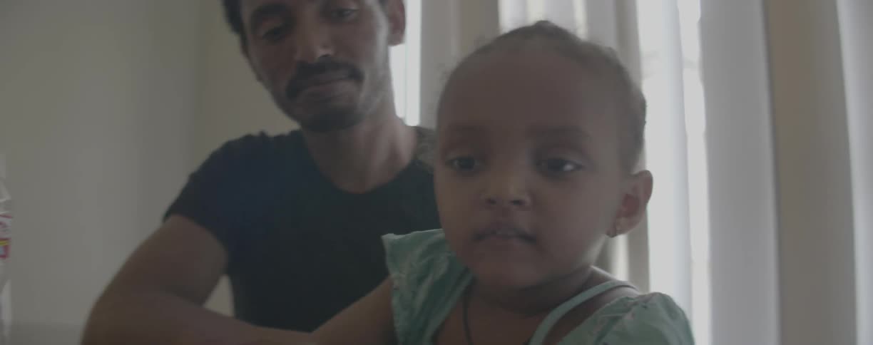 A father sits with his young daughter at home