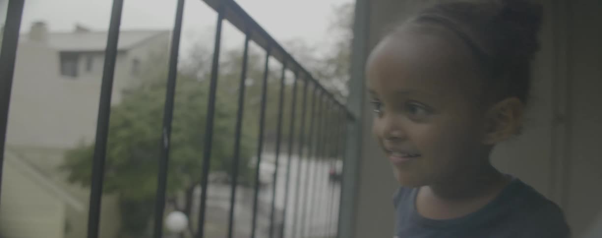 Young girl points as she looks through the bars on the balcony